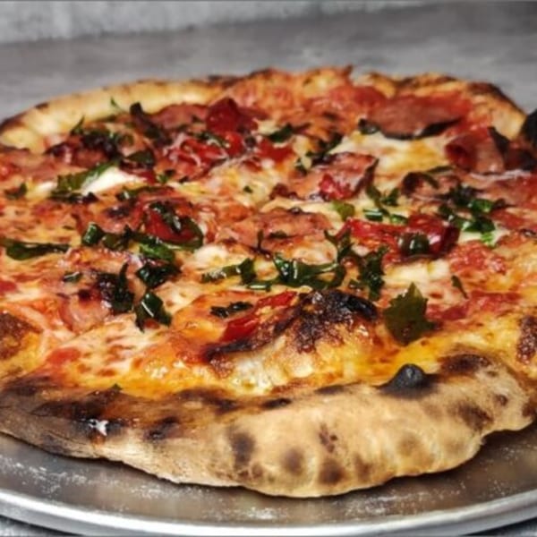 A Fire on the Lake pizza with pepperoni, mozzarella, and fresh basil on a metal tray.