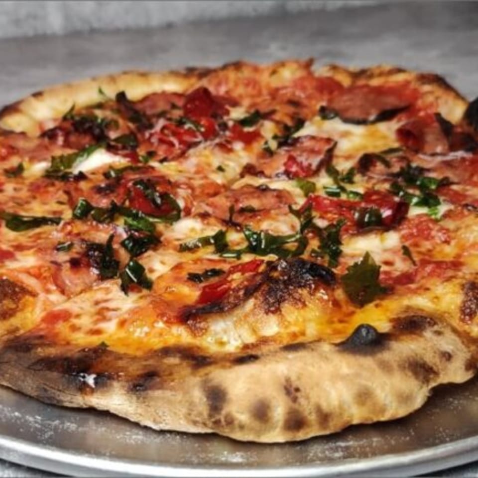 A Fire on the Lake pizza with pepperoni, mozzarella, and fresh basil on a metal tray.