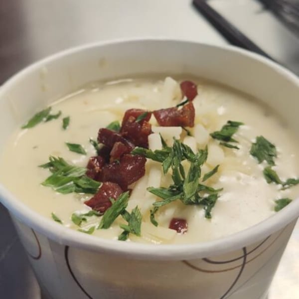 Creamy soup in a white cup, topped with diced bacon, white cheese, and fresh parsley.