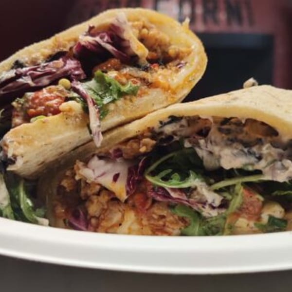 Two pita sandwiches filled with chicken, red cabbage, and arugula, drizzled with sauce.