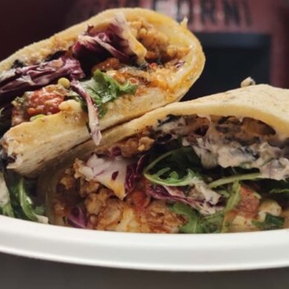 Two pita sandwiches filled with chicken, red cabbage, and arugula, drizzled with sauce.
