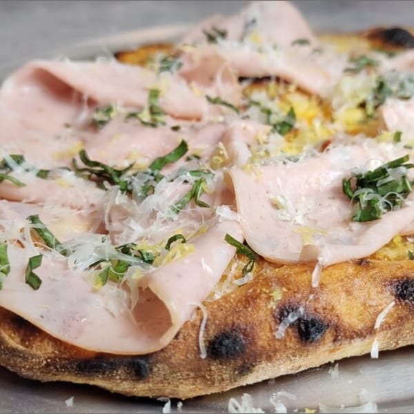Mortadella pizza from Fire on the Lake, topped with shaved cheese and fresh herbs.