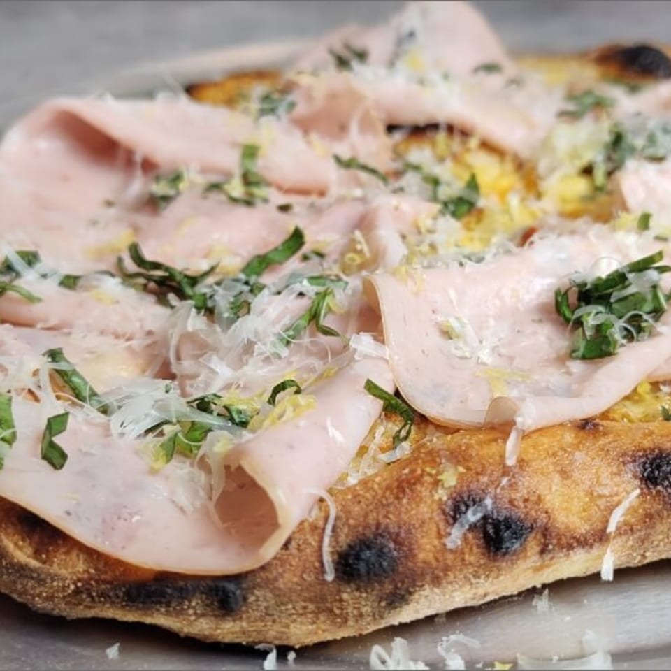 Mortadella pizza from Fire on the Lake, topped with shaved cheese and fresh herbs.