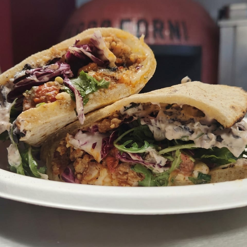 Two halves of a pita sandwich filled with chicken, lettuce, red cabbage, and white sauce.