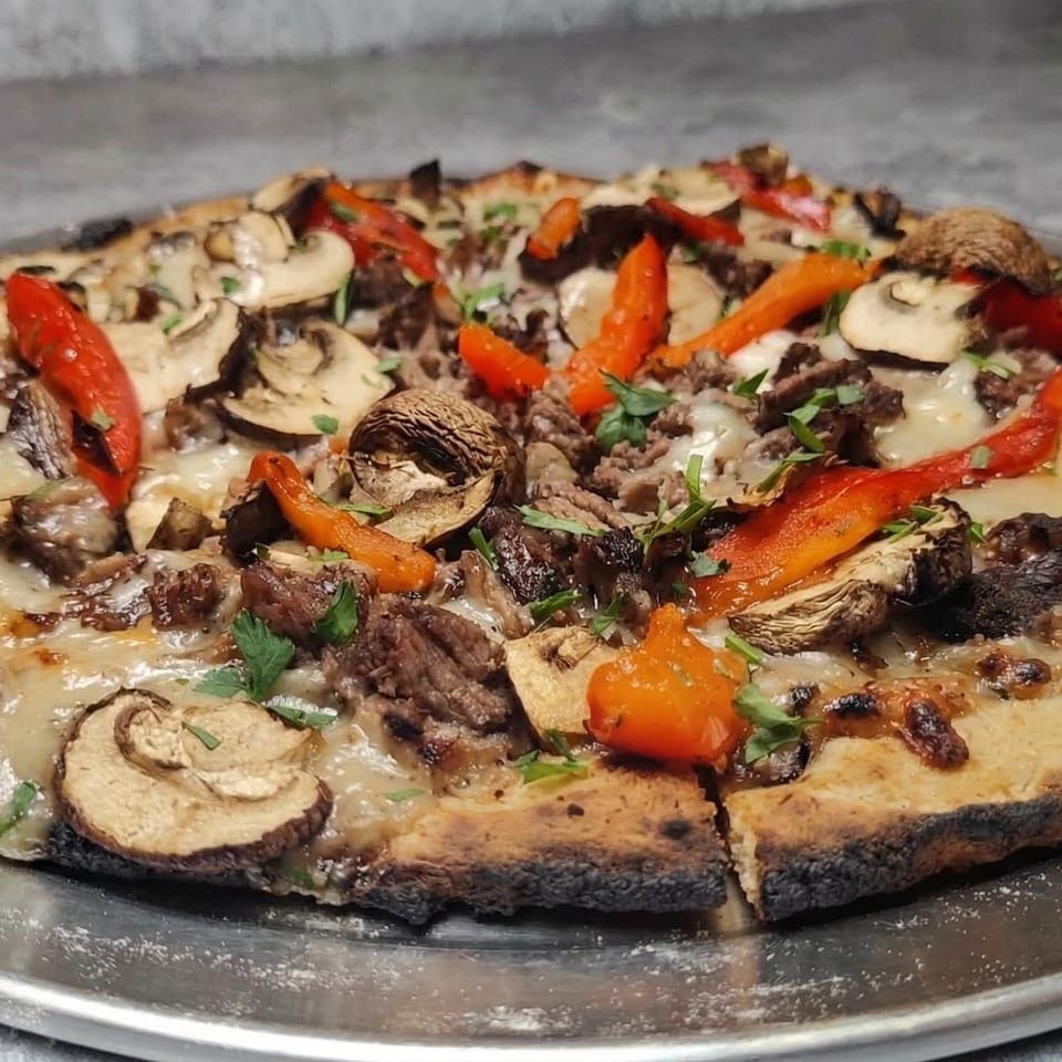 Fire on the Lake pizza with mushrooms, red peppers, and ground meat on a metal tray.