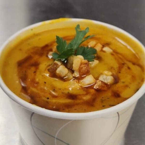 Creamy orange soup with croutons and a sprig of parsley in a white cup.
