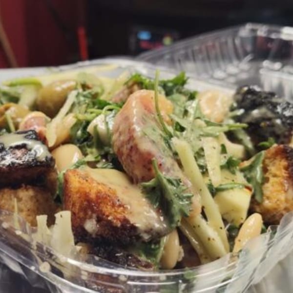 Close-up of a Fire on the Lake salad with greens, white beans, and croutons in a plastic container.