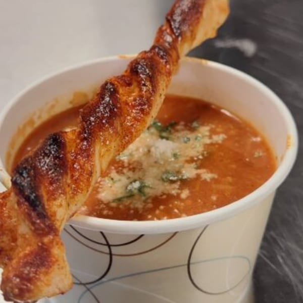 Tomato soup with parmesan cheese and a twisted breadstick in a paper cup.