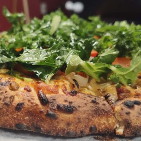 Close-up of a Fire on the Lake pizza with a thick crust, cheese, and fresh green toppings.