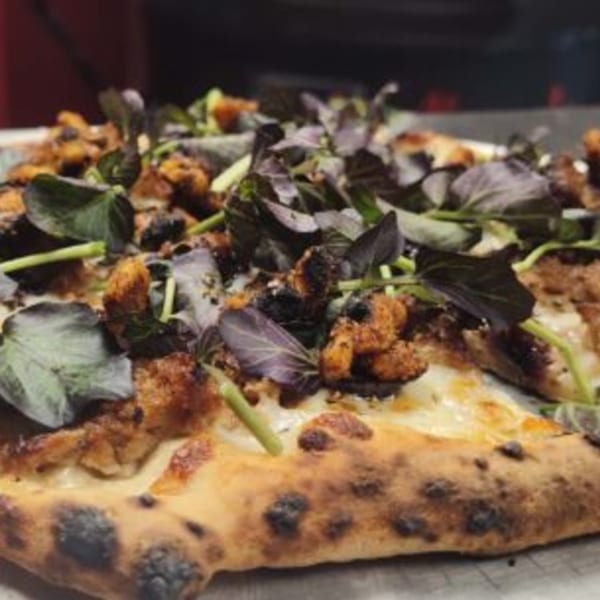 Fire on the Lake pizza with charred crust, melted cheese, chicken, and fresh basil.