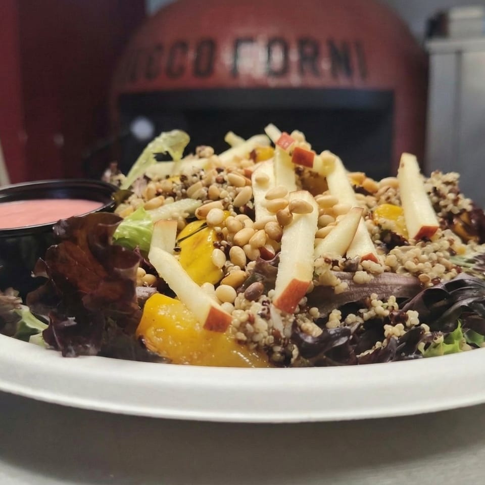 A fresh salad with mixed greens, apples, quinoa, pine nuts, and a side of pink dressing.