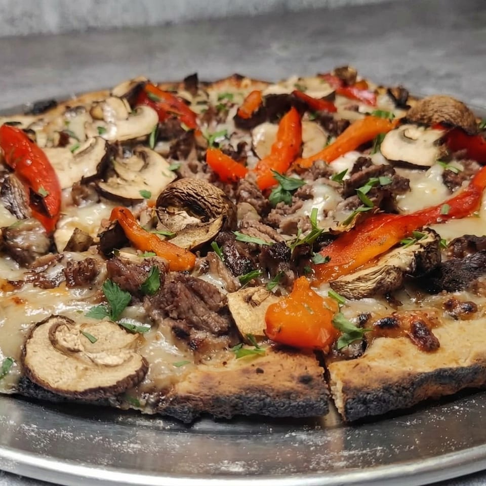 A Fire on the Lake pizza with mushrooms, red peppers, and meat on a metal tray.