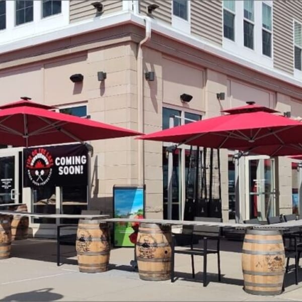 Fire on the Lake pizzeria exterior with red umbrellas, barrel tables, and a "Coming Soon!" banner.