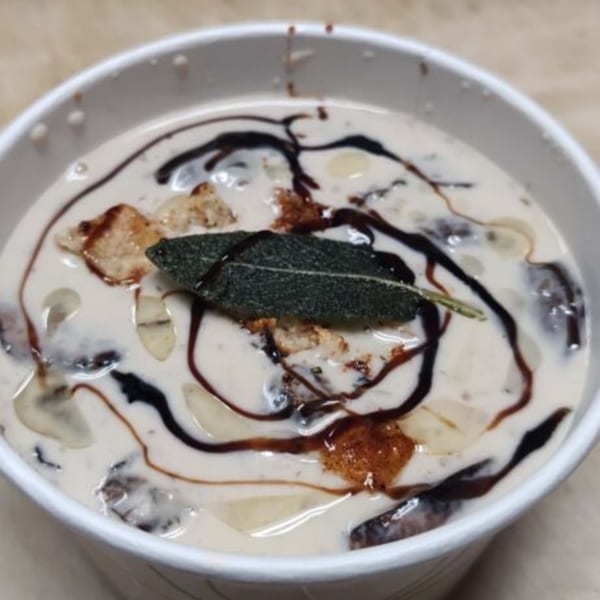 Creamy dessert with dark chocolate drizzle, candied nuts, and a green leaf garnish in a white cup.